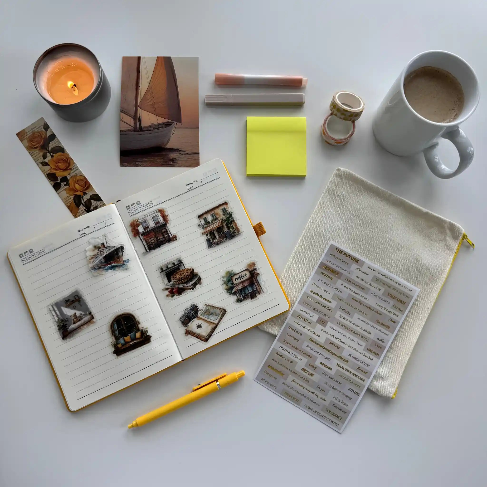 Notebook with stickers, a pen, a mug, a candle, and other items on a white surface