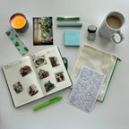 Desk setup with a notebook, mug, candle, and stationery items on a white surface
