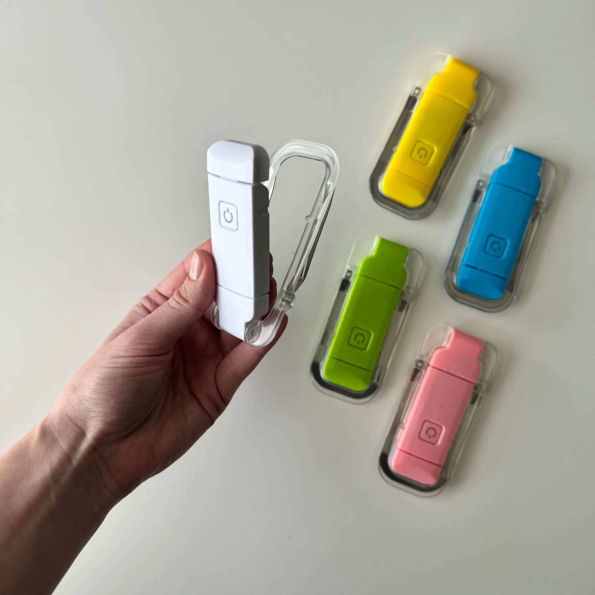 Hand holding a white USB reading light with colorful USB reading lights in clear cases on a light gray background